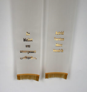 eine Trauerschleife in der Farbe creme mit goldenem Text